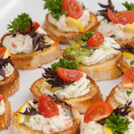 Closeup of delicious canape served on white plate during wedding celebration. Yummy bread with cheese, tomatoes and greens. Concept od catering, appetizer and snack.